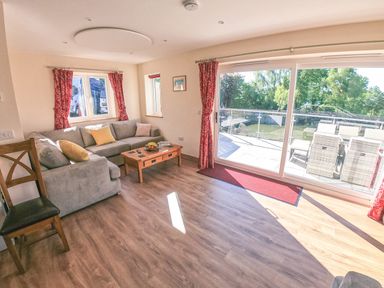 A living room with a gray sofa yellow cushions wooden coffee table and large sliding glass door overlooking an outdoor dining area at Swallows Dip in Honiton
