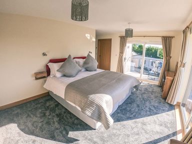 A bedroom with a bed and two pillows near sliding doors and a wooden cabinet at Swallows Dip in Honiton