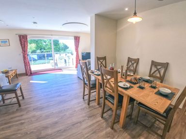 A dining area with a wooden table set for six and a living room with sliding glass doors and red curtains at Swallows Dip in Honiton