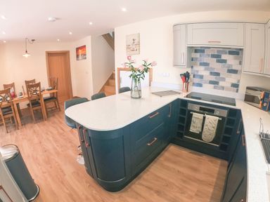 A kitchen with a white countertop island, blue cabinets, a built-in oven, and a dining table with chairs at Swallows Dip in Honiton