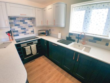 A kitchen with blue and white cabinets a stove sink and microwave at Swallows Dip in Honiton