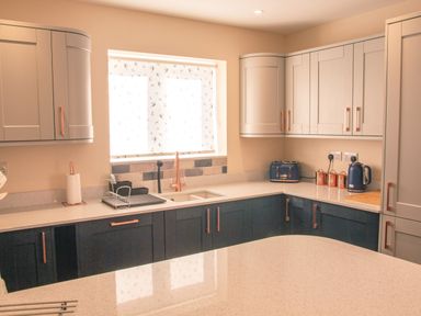 A kitchen with two-tone cabinets a window with patterned blinds a sink and countertop appliances at Swallows Dip in Honiton
