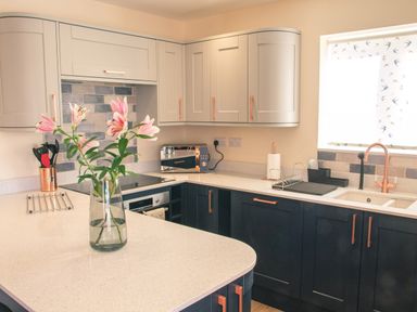 A kitchen with light and dark cabinetry a vase with pink flowers microwave and a sink by a window at Swallows Dip in Honiton