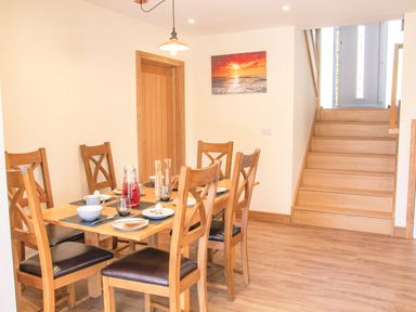A dining area with a wooden table and six chairs set with plates cups and glasses near staircase at Swallows Dip in Honiton