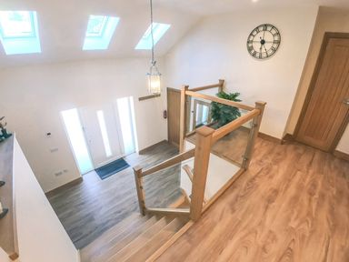 A staircase with wooden and glass railing overlooking an entrance with a door and skylights at Swallows Dip in Honiton