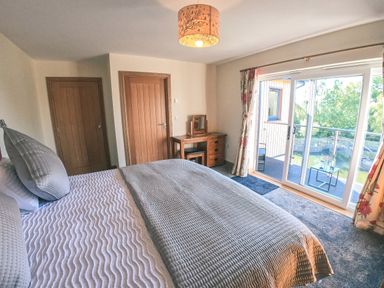 A bedroom with a bed grey bedding wooden doors a wooden desk and glass sliding doors leading to a balcony at Swallows Dip in Honiton