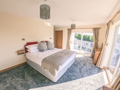 A bedroom with a double bed gray carpet and sliding glass doors at Swallows Dip in Honiton