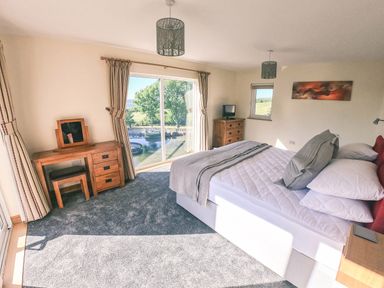 A bedroom with a bed a wooden dressing table and a chest of drawers with windows and curtains at Swallows Dip in Honiton