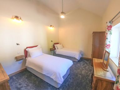 A bedroom with two single beds a wooden dresser a mirror and a wardrobe at Swallows Dip in Honiton