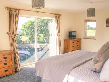 A bedroom with a bed beside a sliding glass door and wooden furniture at Swallows Dip in Honiton