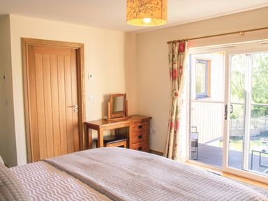 A bedroom with a bed a wooden door a wooden desk with a mirror and a sliding glass door with floral curtains at Swallows Dip in Honiton