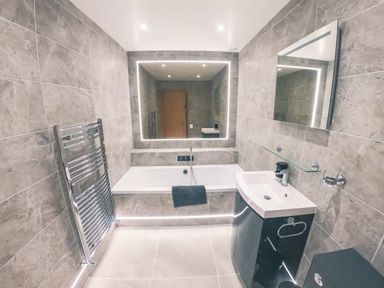 A bathroom with a bathtub a sink a black cabinet a heated towel rack and two mirrors at Swallows Dip in Honiton