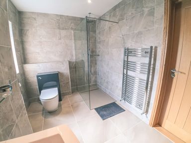 A bathroom with a toilet a glass shower area a chrome towel radiator and a wooden door at Swallows Dip in Honiton