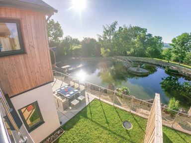 A backyard with outdoor dining table and chairs next to a pond with a wooden bridge at Swallows Dip in Honiton
