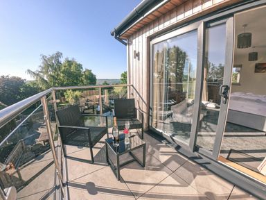 A balcony with two black chairs and a small glass table with a bottle and glass near glass sliding doors at Swallows Dip in Honiton