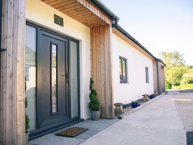 The exterior of a house with a black front door and potted plants at Swallows Dip in Honiton