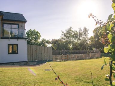 A house with a balcony and fenced garden area with trees and grass at Swallows Dip in Honiton