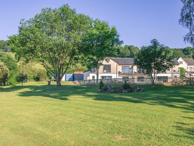 A large grass lawn with several trees and a fenced area near a modern house at Swallows Dip in Honiton