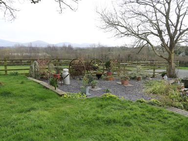 A garden area with a large tree potted plants gravel and wooden fence with mountains in the background at Trem Y Wyddfa in Gaerwen