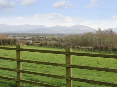 A green field with a wooden fence in the foreground and hills in the background at Trem Y Wyddfa in Gaerwen