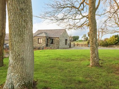 A stone house with a slate roof behind trees and a grassy area at Trem Y Wyddfa in Gaerwen