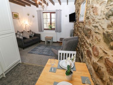 A living room with a gray sofa, armchair, small wooden tables, wall-mounted TV, and a dining table with plates and a plant on it at Trem Y Wyddfa in Gaerwen