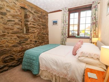 A bedroom with a stone wall a bed with white and teal bedding a window and floral curtains at Trem Y Wyddfa in Gaerwen