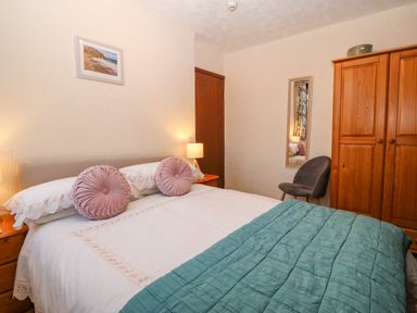 A bedroom with a bed covered with pillows and a blanket a wooden wardrobe and a chair at Trem Y Wyddfa in Gaerwen