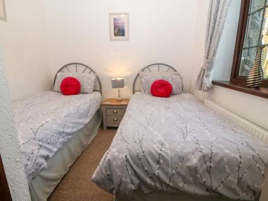 A bedroom with two single beds a nightstand with a lamp between the beds and a window with curtains at Trem Y Wyddfa in Gaerwen
