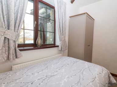 A bedroom with a bed covered in patterned bedding next to a window with curtains and a wardrobe in the corner at Trem Y Wyddfa in Gaerwen