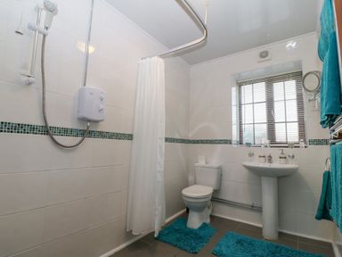 A bathroom with a shower area toilet pedestal sink window and blue rugs and towels at Trem Y Wyddfa in Gaerwen
