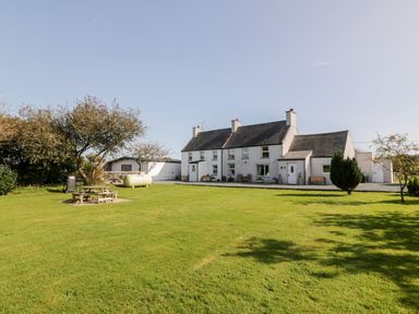 A large grassy yard with picnic table trees and a two-story house with white walls and gray roof at Penllyn in Newborough