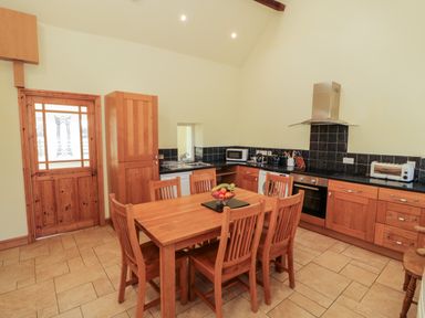 A kitchen with wooden cabinets a dining table with six chairs and fruit bowl at Penllyn in Newborough