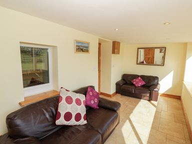 A room with two brown leather sofas with patterned cushions a window a mirror on the wall and tiled floor at Penllyn in Newborough