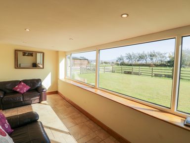 A sitting room with two leather sofas and a large window showing a garden and fenced field at Penllyn in Newborough