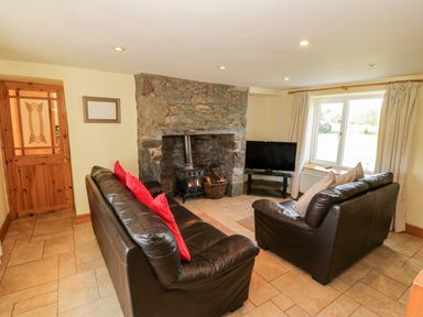 A living room with two brown leather sofas a stone fireplace and a television near a window at Penllyn in Newborough