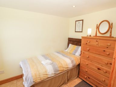 A bedroom with a single bed beside a wooden dresser with a mirror and a lamp at Penllyn in Newborough