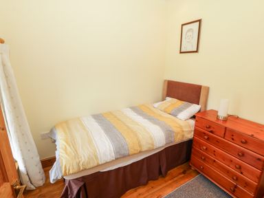 A single bed with striped bedding next to a wooden dresser with a lamp in a small bedroom at Penllyn in Newborough
