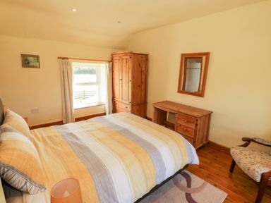 A bedroom with a bed with striped bedding a wooden wardrobe a desk with a mirror and a chair at Penllyn in Newborough