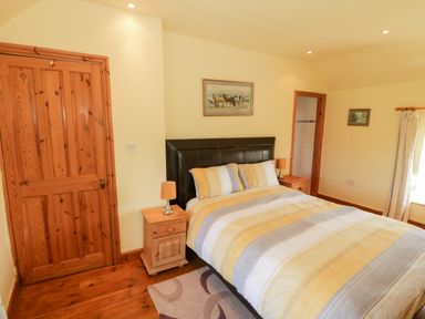 A bedroom with a double bed with striped bedding two wooden nightstands with lamps a wooden door and framed pictures on the wall at Penllyn in Newborough