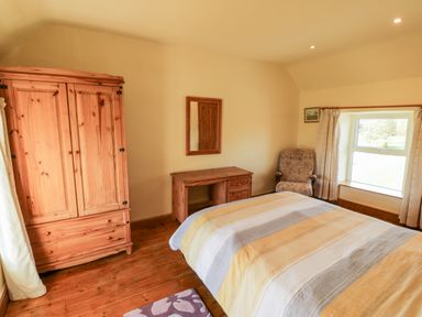 A bedroom with a bed a wooden wardrobe a wooden desk an armchair and a window at Penllyn in Newborough