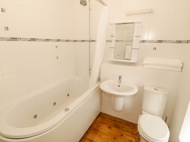 A bathroom with a bathtub shower sink toilet and folded towels on a shelf at Penllyn in Newborough