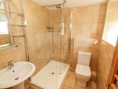 A bathroom with a sink, glass shower enclosure, and toilet at Penllyn in Newborough