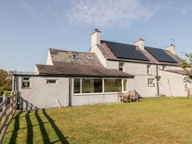 A house with solar panels on the roof a wooden fence and chairs on the lawn at Penllyn in Newborough