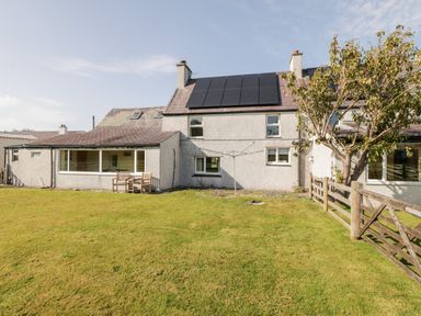 A backyard with green grass a tree wooden fence two chairs and a house with solar panels on the roof at Penllyn in Newborough