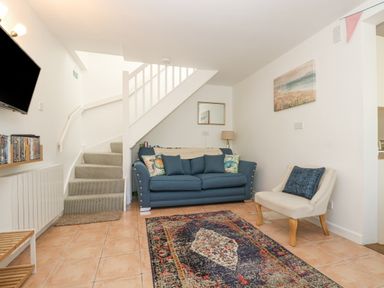 A living room with a blue sofa a beige chair a patterned rug and a staircase at Longships in Porthcurno