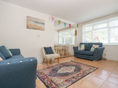 A living room with blue sofas a patterned rug and a small dining table with chairs at Longships in Porthcurno