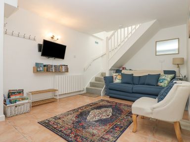 A living room with a blue sofa an armchair a wall-mounted TV and a staircase at Longships in Porthcurno