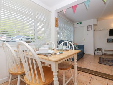 A dining table with four chairs set with bowls and glasses next to a living area with a blue sofa at Longships in Porthcurno