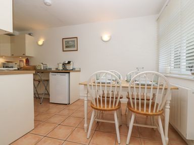 A kitchen dining area with a wooden table and four white chairs with wooden seats at Longships in Porthcurno